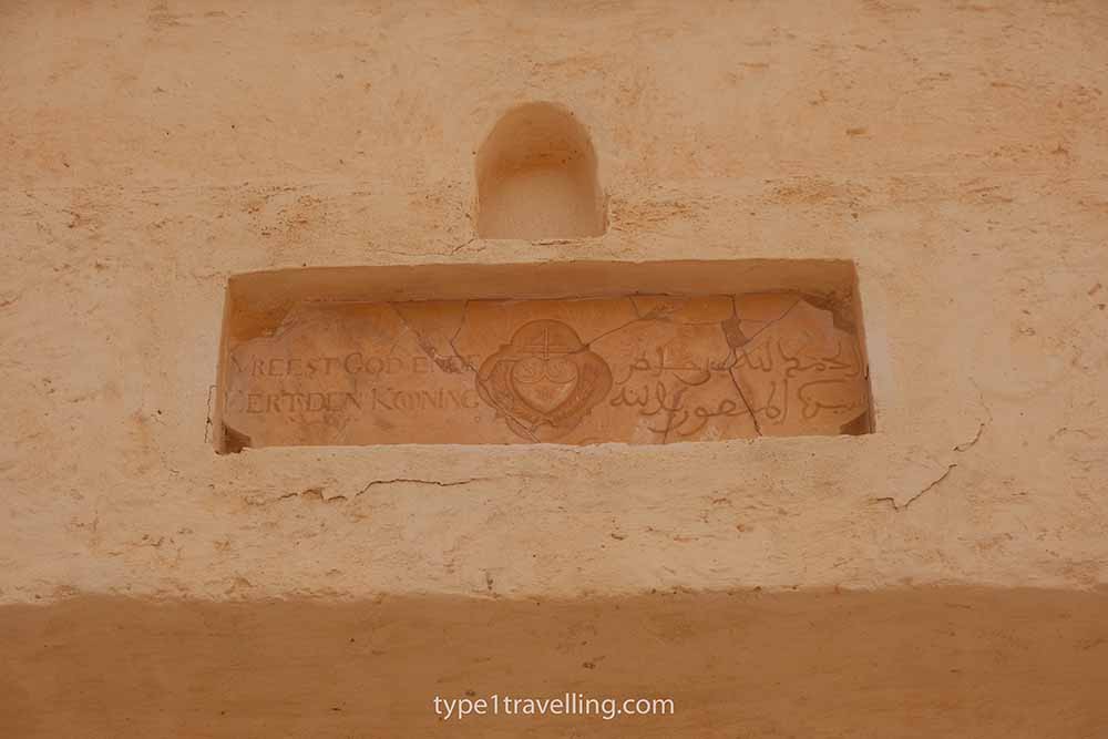 agadir-kasbah-marble-cartouche A cracked plaque with a symbol in the middle, a Dutch inscription on the left, and an Arabic inscription on the right.