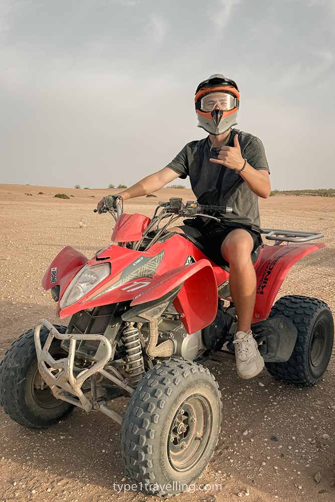 A person sitting on a quad bike with a full face helmet making a gesture with one hand.