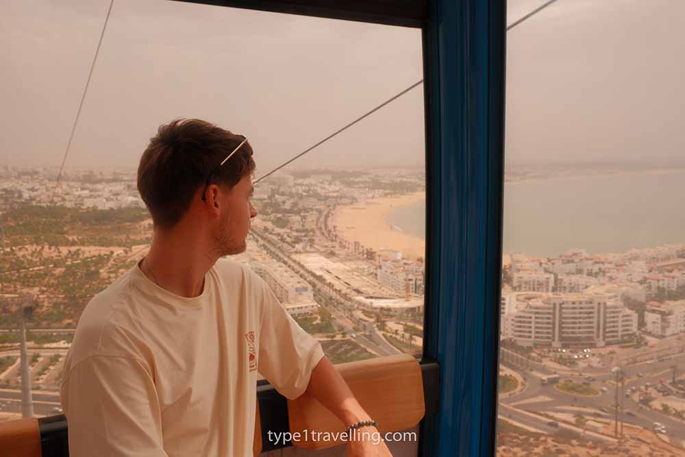 inside-agadir-cable-car A man looking out of the cabin on the Agadir Cable Car over the beach and city below.