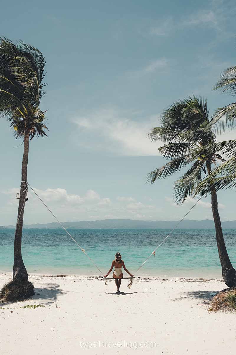 Lucy sitting on a swing between two palm trees on Leela Beach.