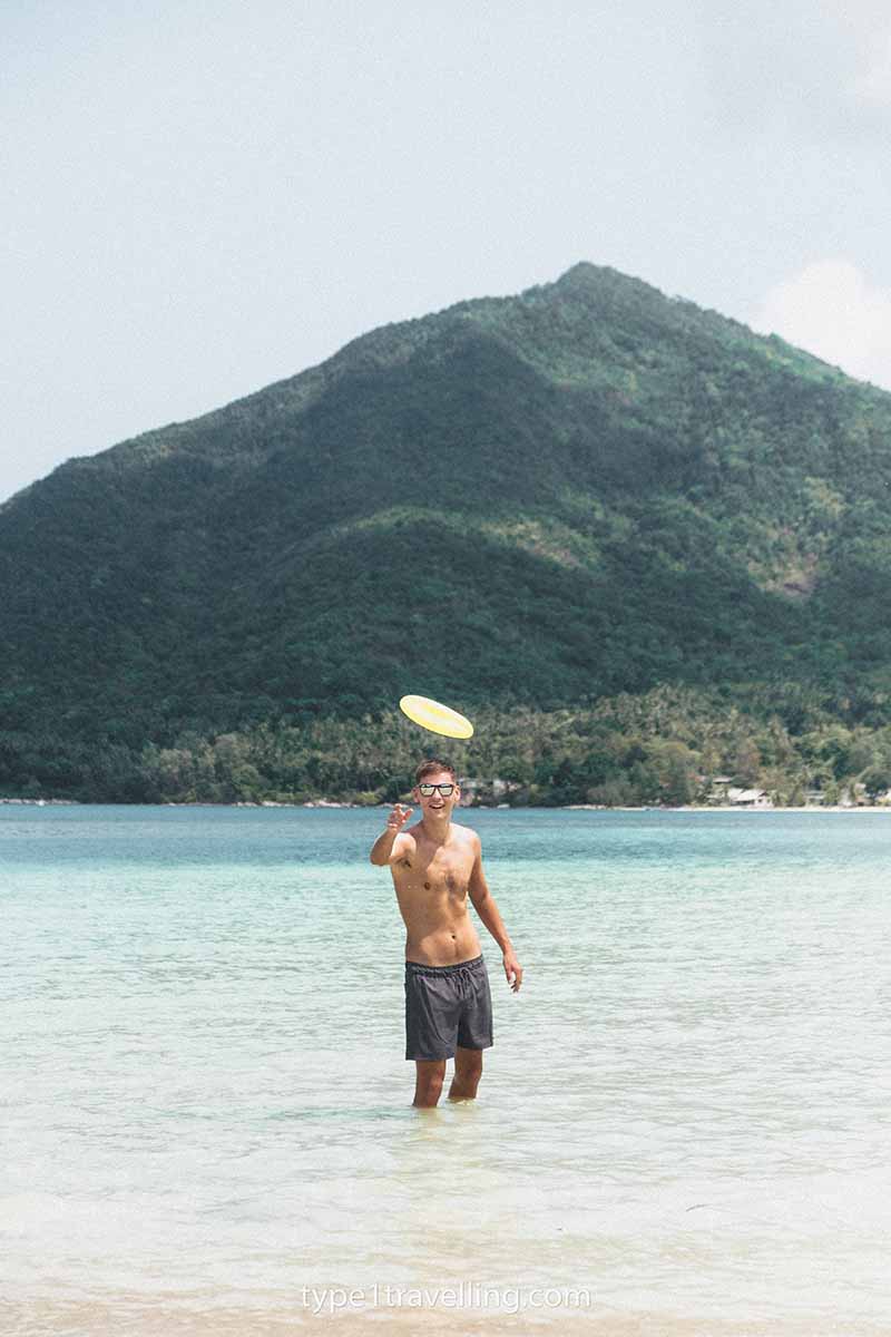 Sam throwing a frisbee while standing knee-deep in the sea at Malibu Beach with a towering, pointed mountain in the background.