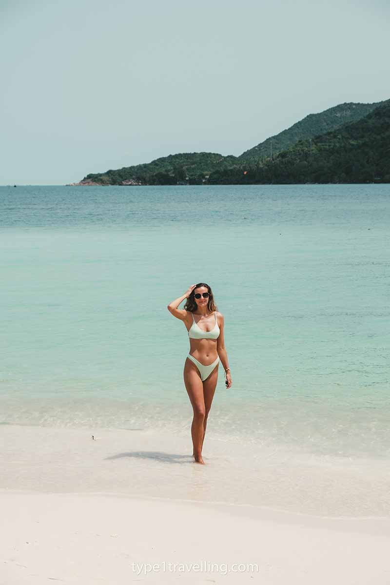 Lucy standing ankle deep in water on the shoreline of Malibu Beach with the north coast of Koh Phangan in the background.