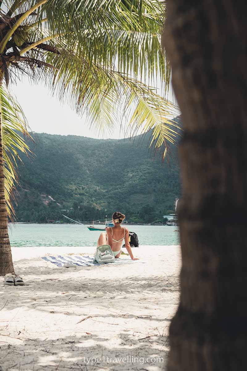 Lucy sunbathing next to a palm tree on Malibu Beach with the Koh Phangan mountains in the distance.