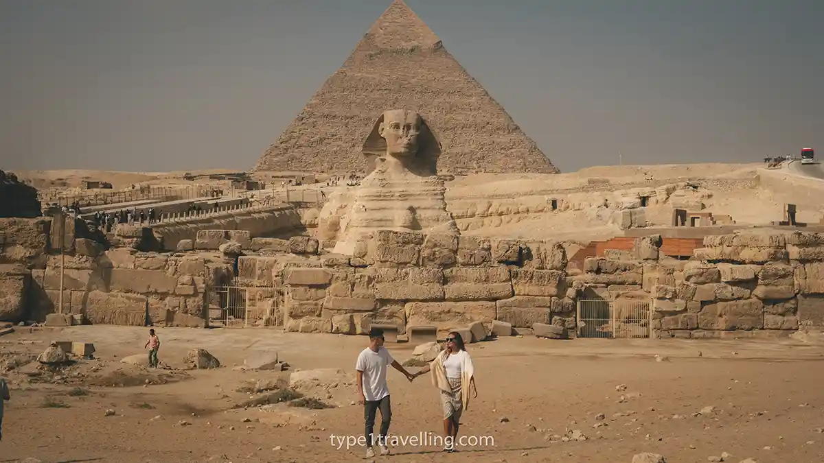 sam-and-lucy-pyramids Sam and Lucy holding hands while walking towards the camera with the Pyramid of Khafre and Great Sphinx of Giza in the background.