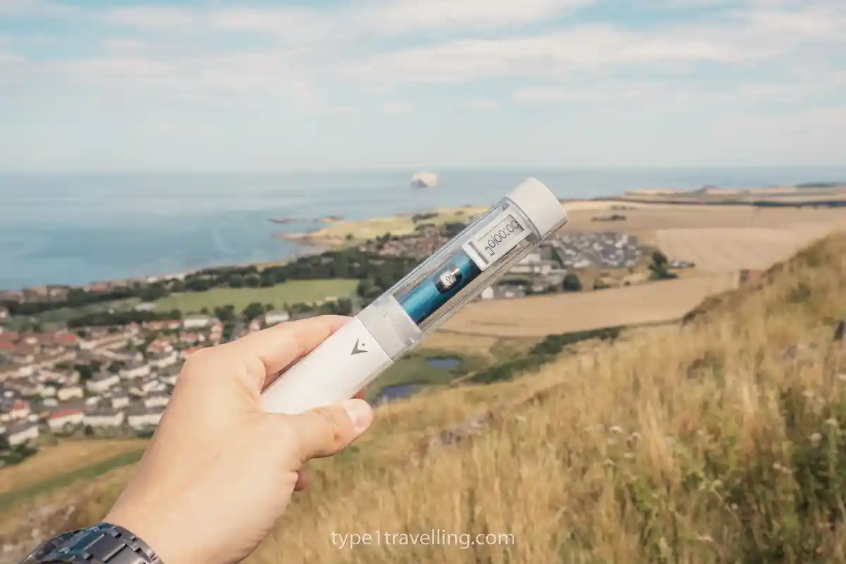 A hand holding a TempraMed VIVI Cap insulin case with a scenic coastal background.