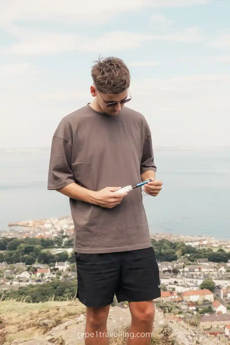Sam standing on a hill overlooking North Berwick inserting an insulin pen into a VIVI Cap case.